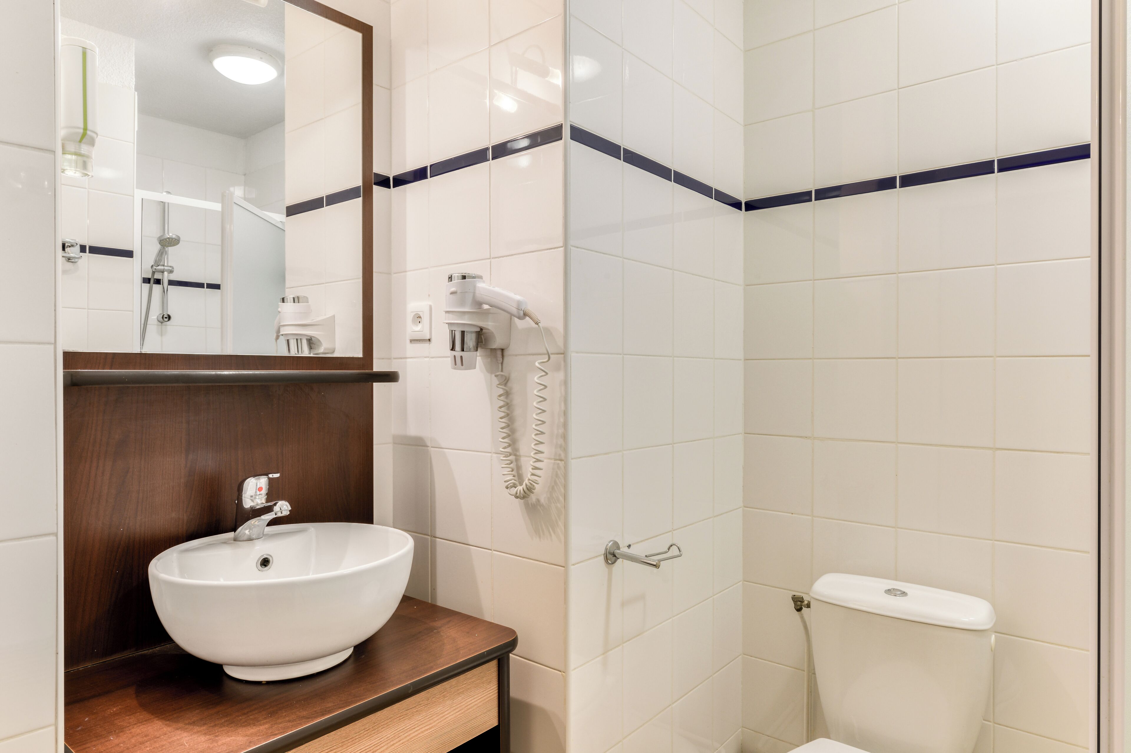 A bathroom with a white sink, a mirror, a hairdryer, and a toilet.