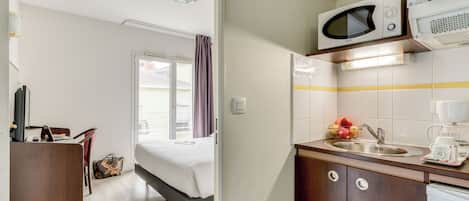 Une chambre d’hôtel équipée d’un lit, d’un bureau et d’une kitchenette avec un four à micro-ondes et une machine à café.