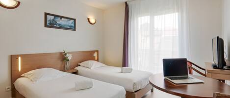 A hotel room with two beds, a desk with a laptop, a TV, and a painting on the wall.