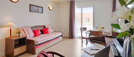 A modern hotel room with a sofa, a desk with a laptop, a dining table, and a balcony with a view.