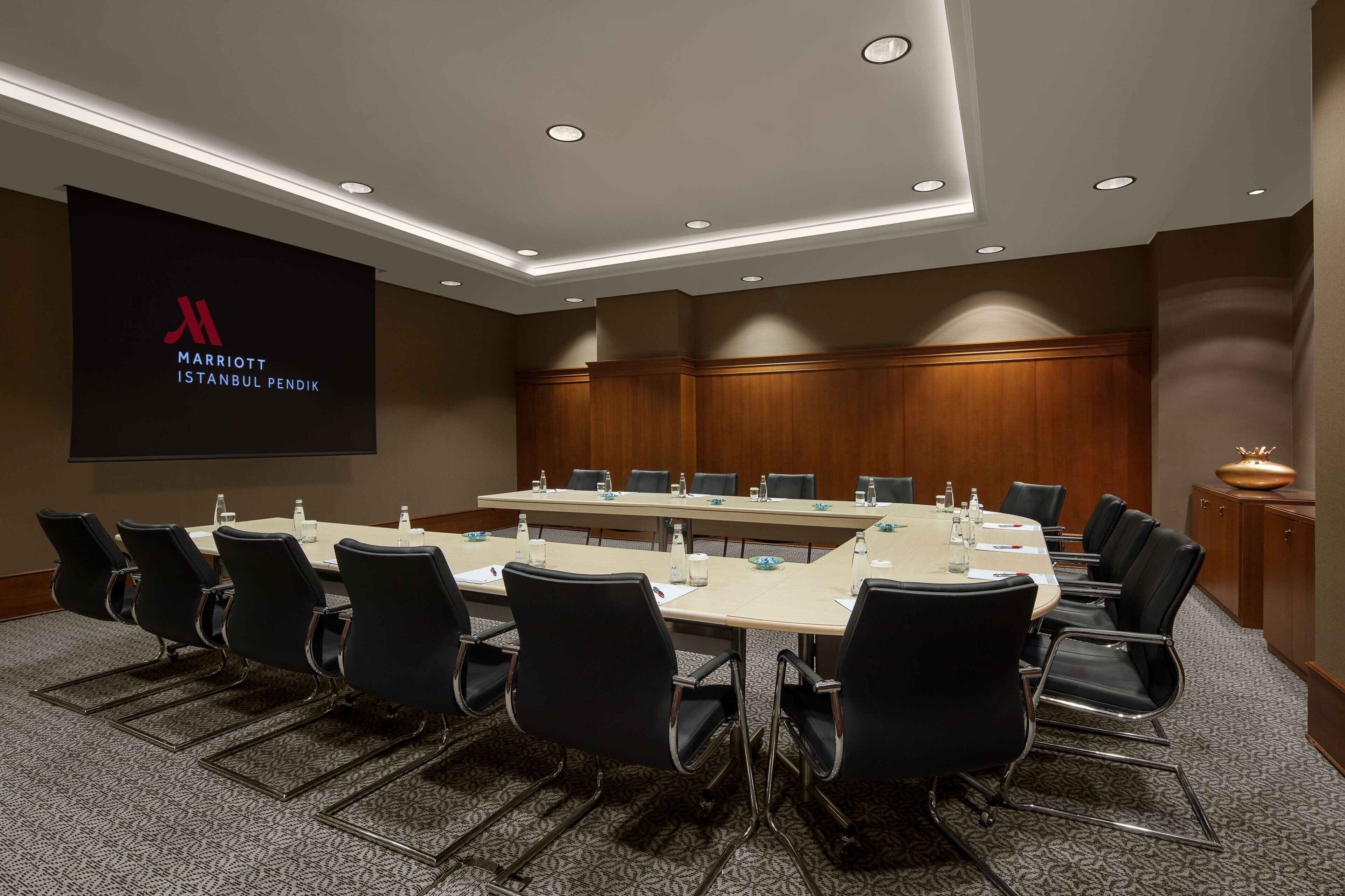 A conference room with a long table, black chairs, and a projector screen displaying the Marriott Istanbul Pendik logo.