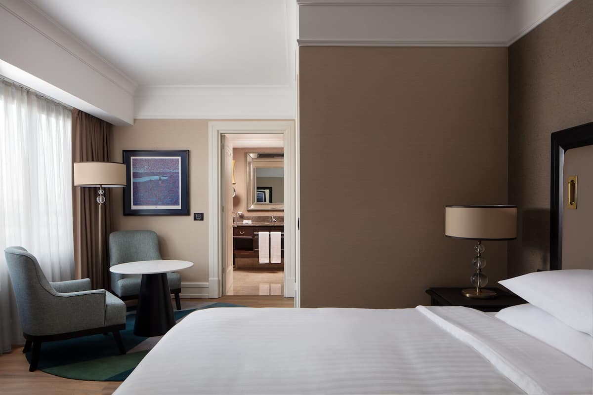A hotel room with a bed, a desk, a chair, a lamp, and a bathroom visible through an open door.