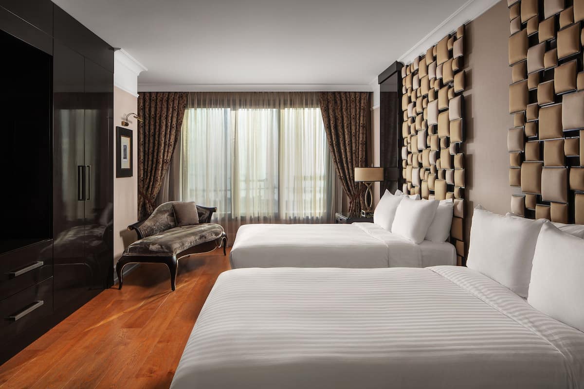A hotel room with two beds, a sofa, a TV, and a wall with a geometric pattern.