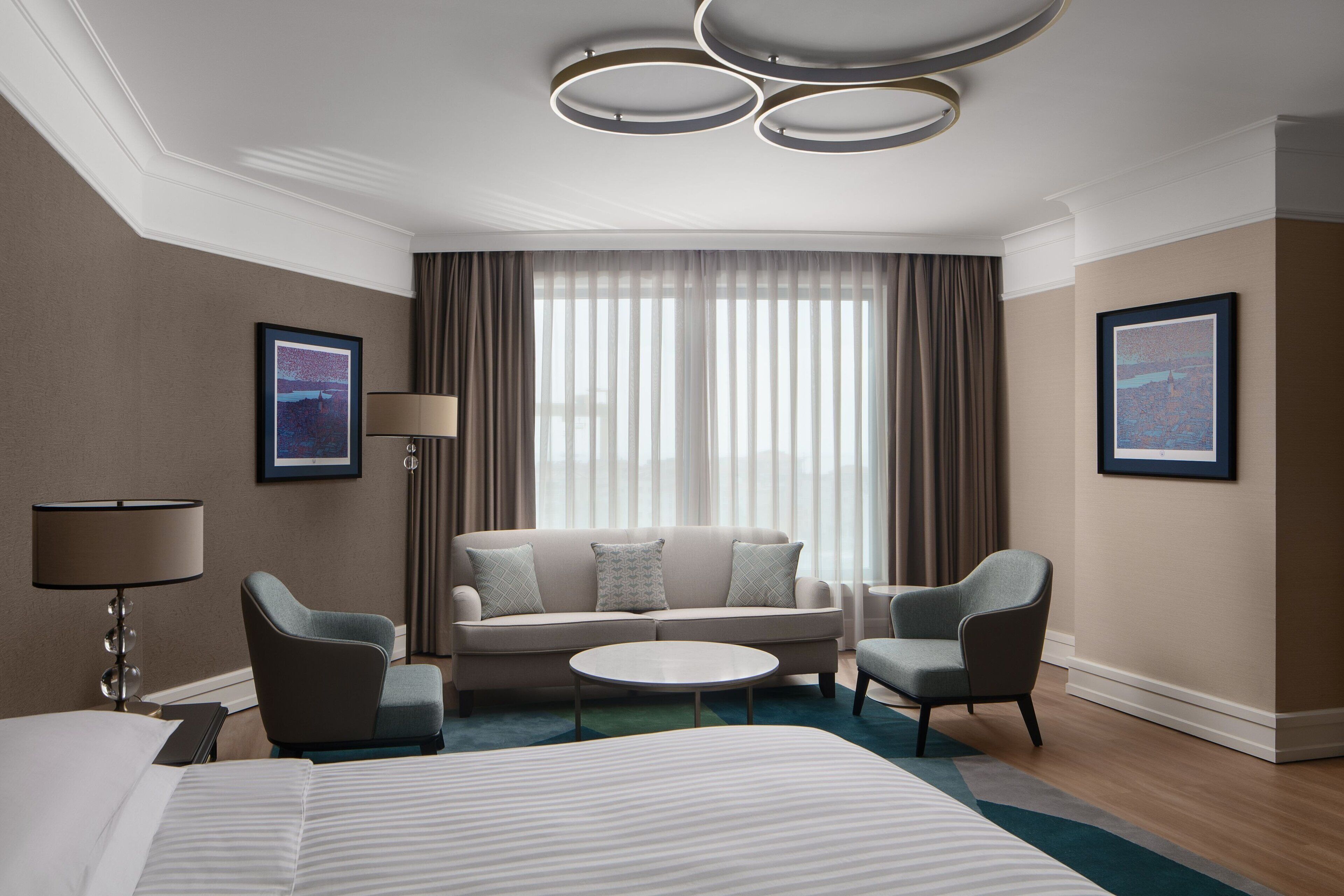 Una habitación de hotel con una cama grande, un sofá, dos sillones, una mesa de centro y una lámpara de pie.