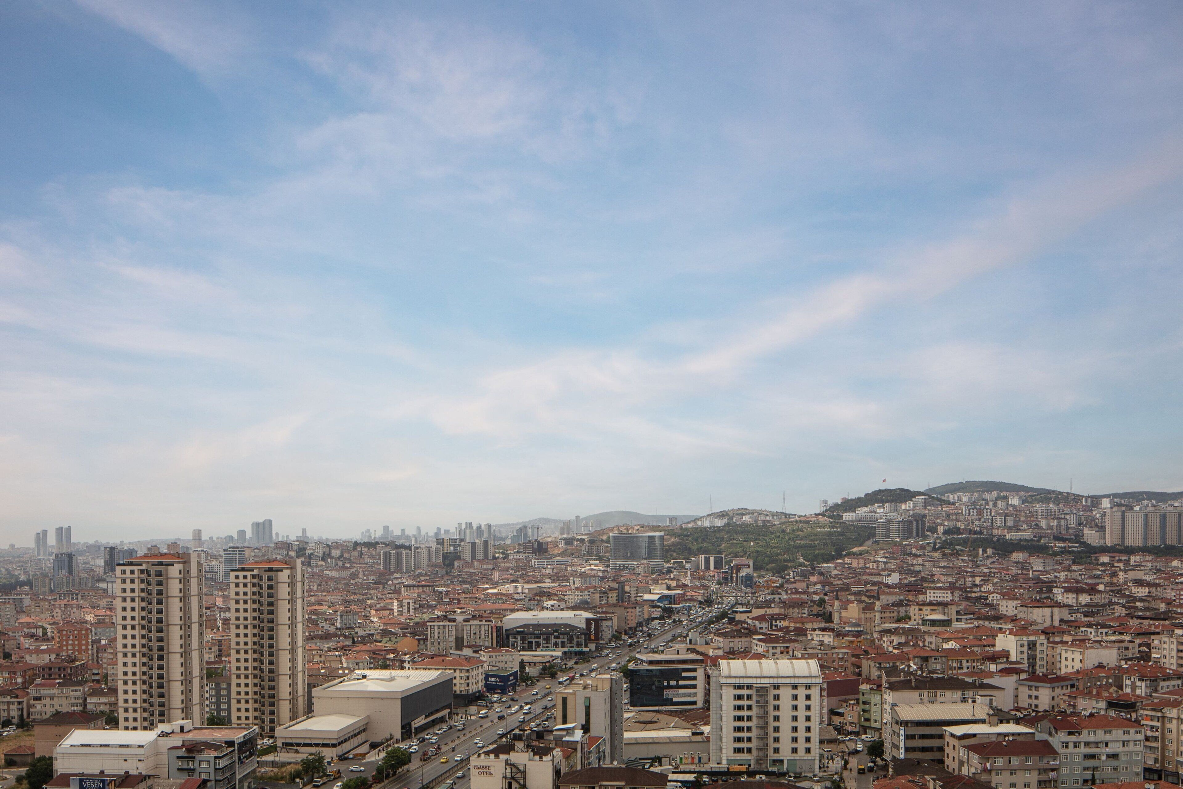 Un paisaje urbano con edificios altos, una combinación de estructuras residenciales y comerciales, y un fondo montañoso.