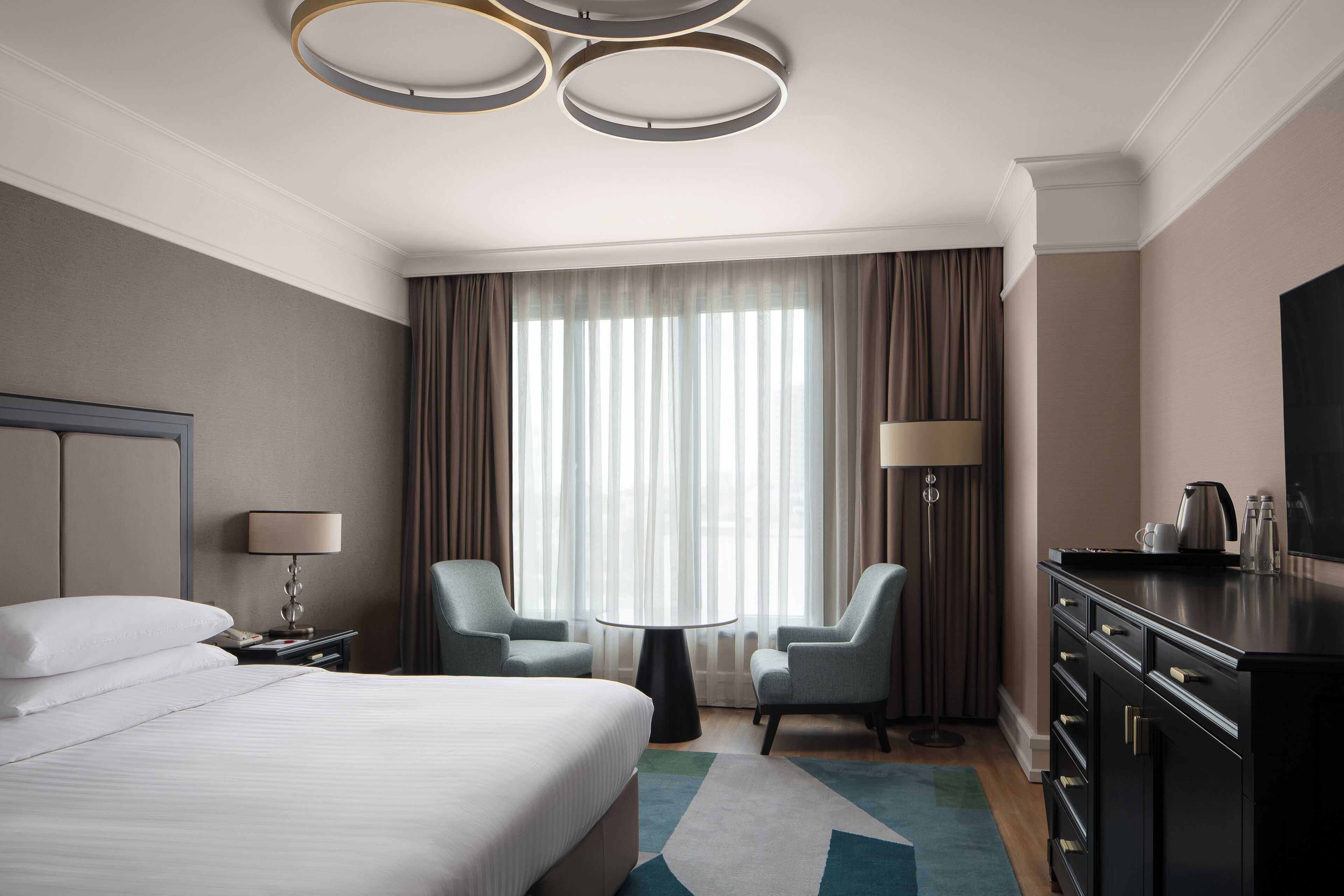 Habitación de hotel con una cama grande, dos sillones, una mesa redonda, un televisor y un minibar.