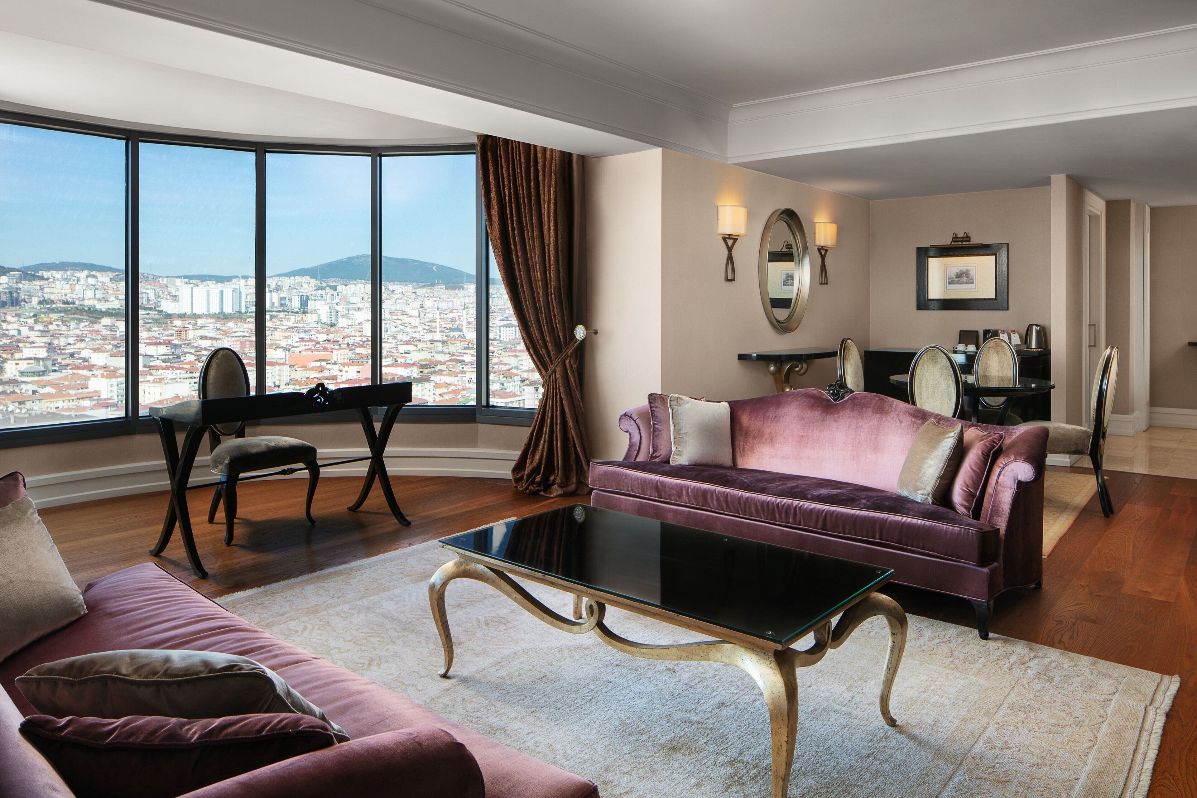 Un vaste salon doté d’une grande fenêtre donnant sur la ville, d’un confortable canapé violet, d’une table basse en verre et d’un coin repas avec une table et des chaises.