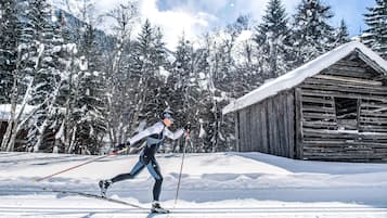 A cross-country skier in a snowy forest with a wooden cabin in the background.