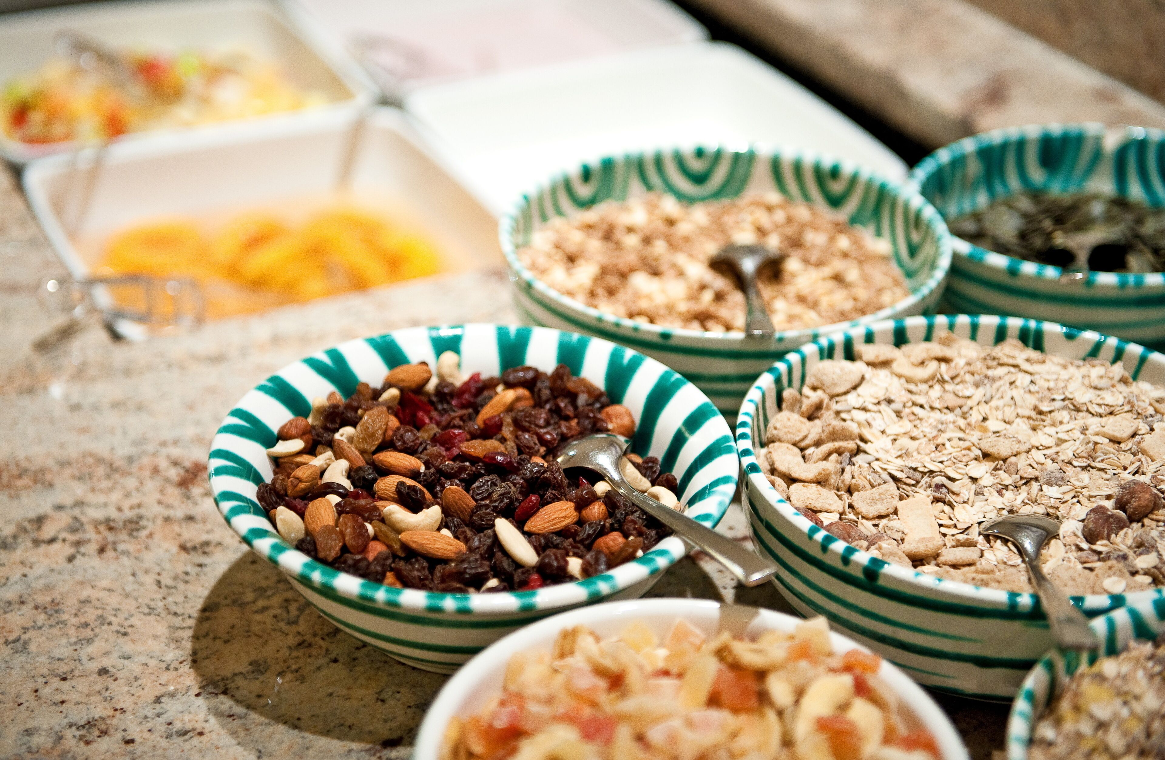 Una variedad de recipientes con diferentes tipos de alimentos, como nueces, frutas secas y cereales, dispuestos sobre una encimera.