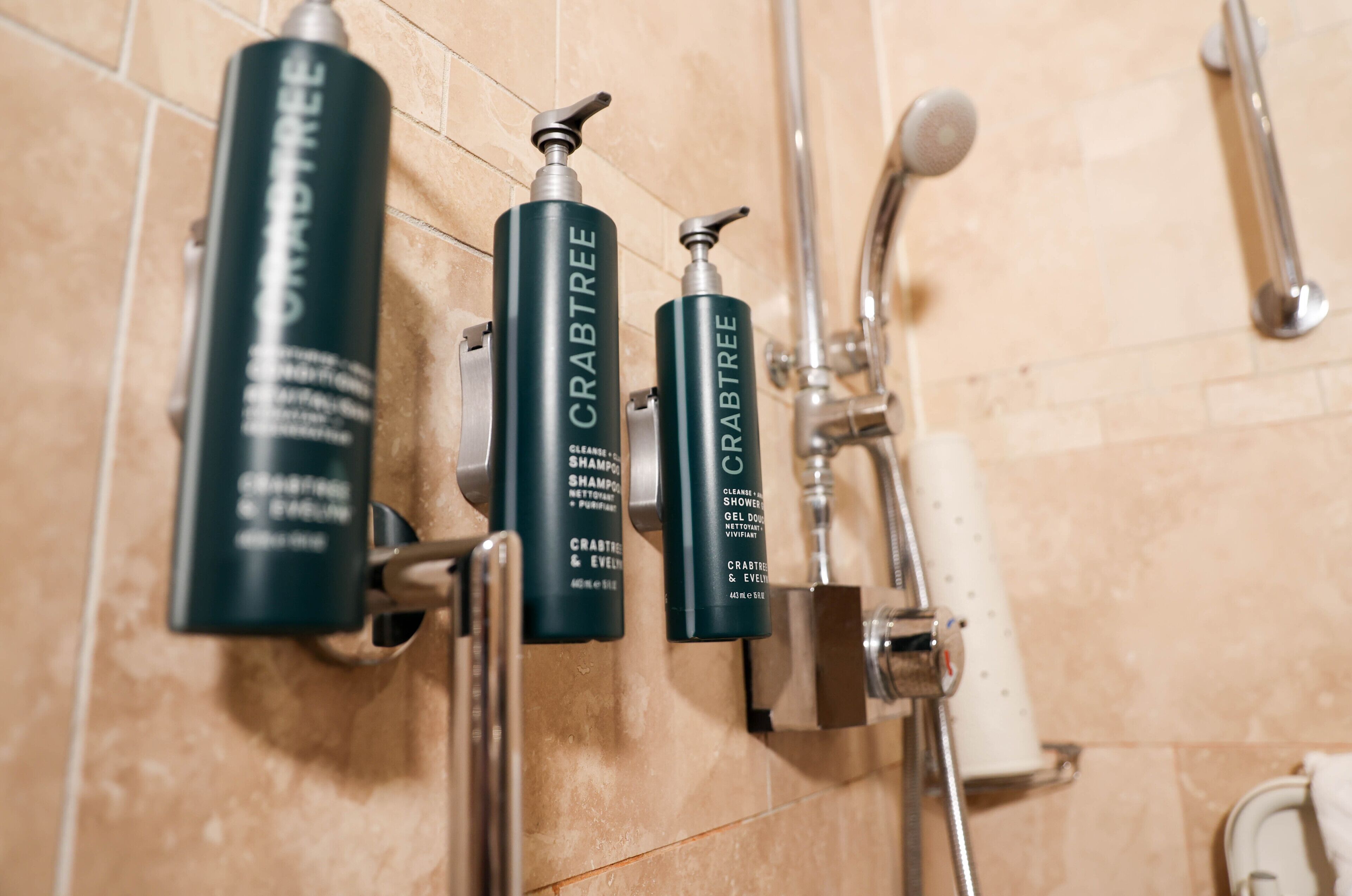 A bathroom with three bottles of Crabtree shampoo and a showerhead.