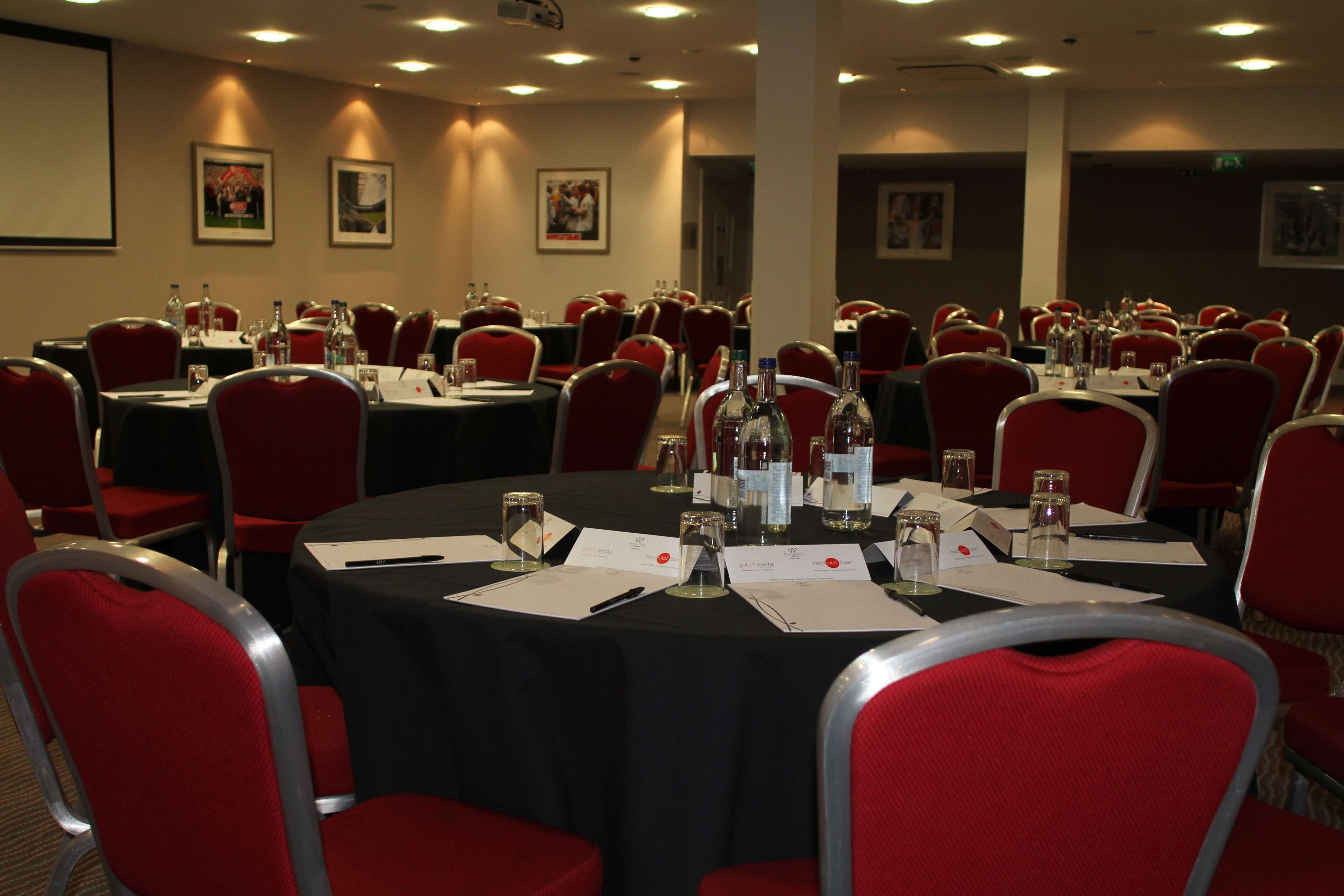 A conference room with round tables, red chairs, and various items like water bottles and papers.