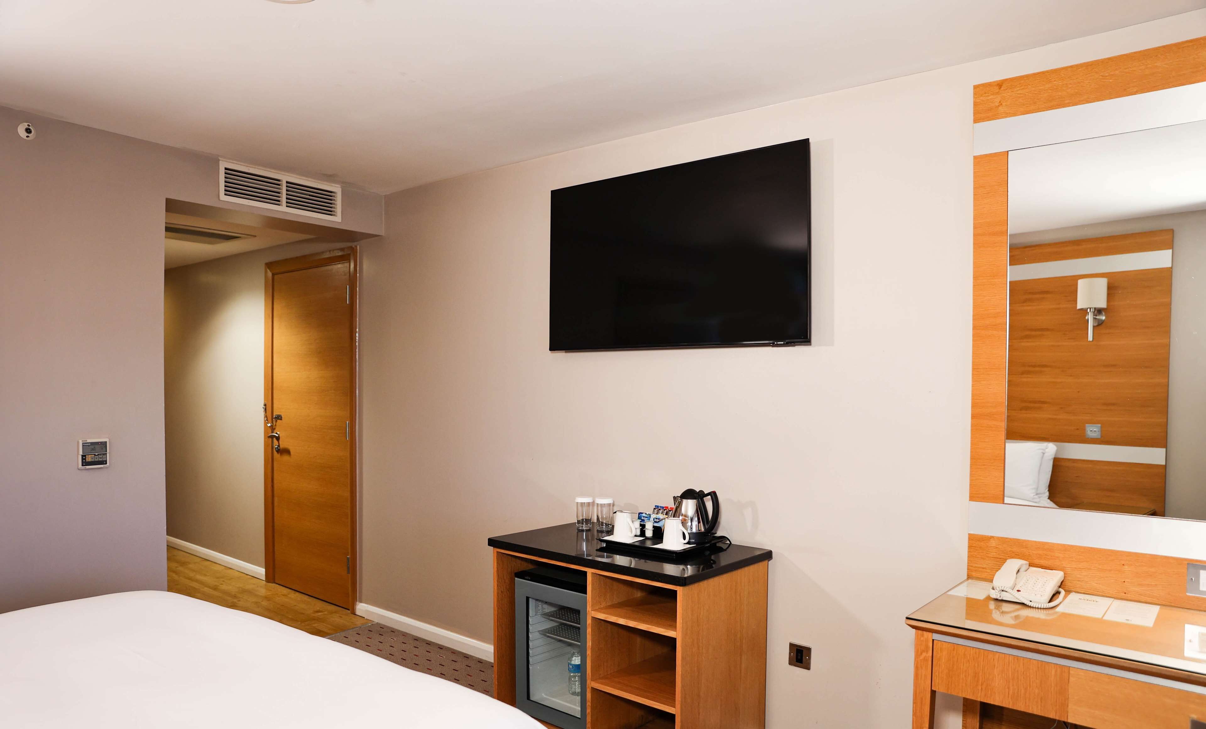 Hotelkamer met een bed, een kleine kitchenette, een televisie, een spiegel en een deur naar een andere kamer.