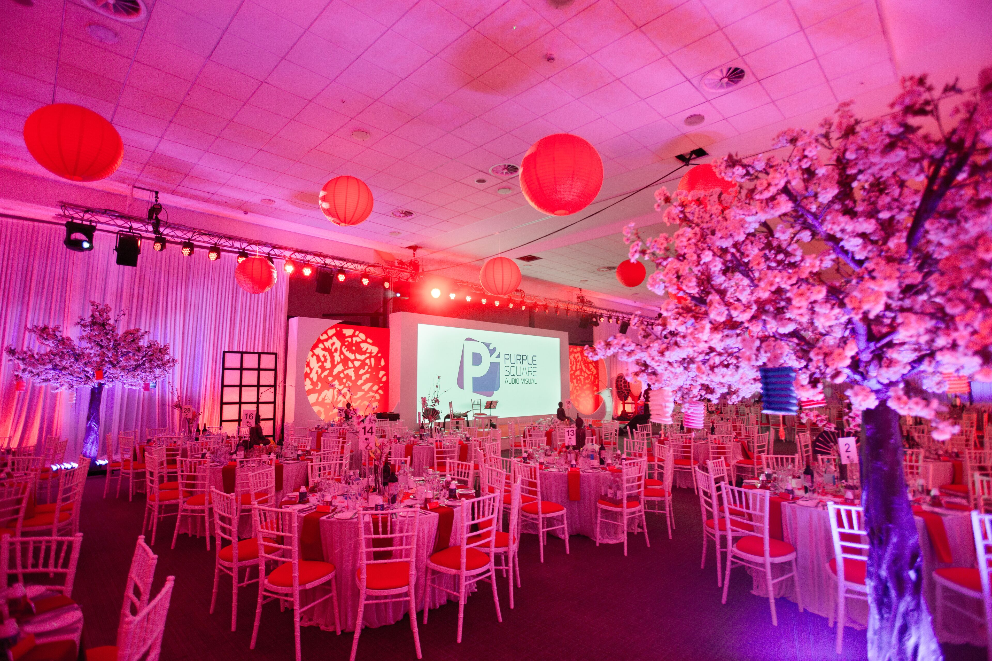 A banquet hall with round tables, white chairs, and red accents.
