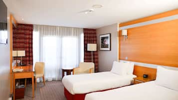 A hotel room with two beds, a desk, a chair, a small table, and a lamp.