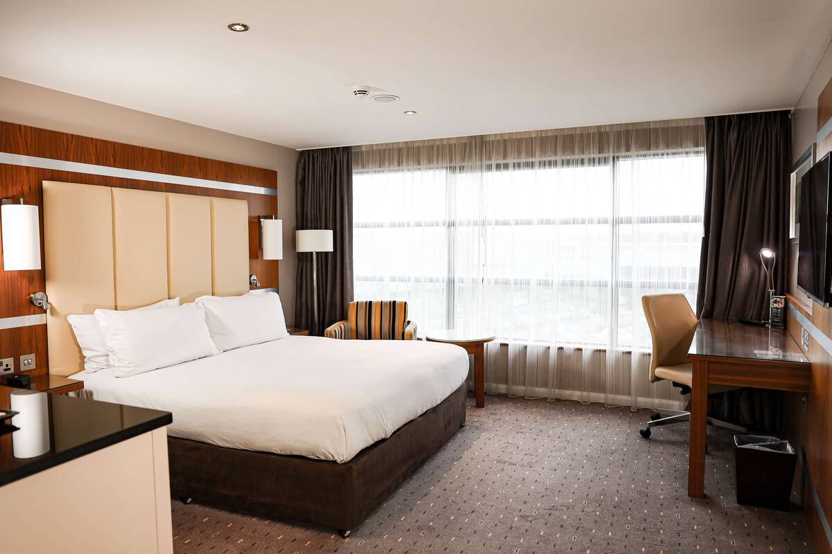 A hotel room with a large bed, a desk, a chair, and a TV.