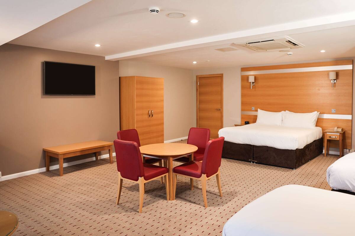 A hotel room with a bed, a desk, two chairs, a TV, and a wardrobe.