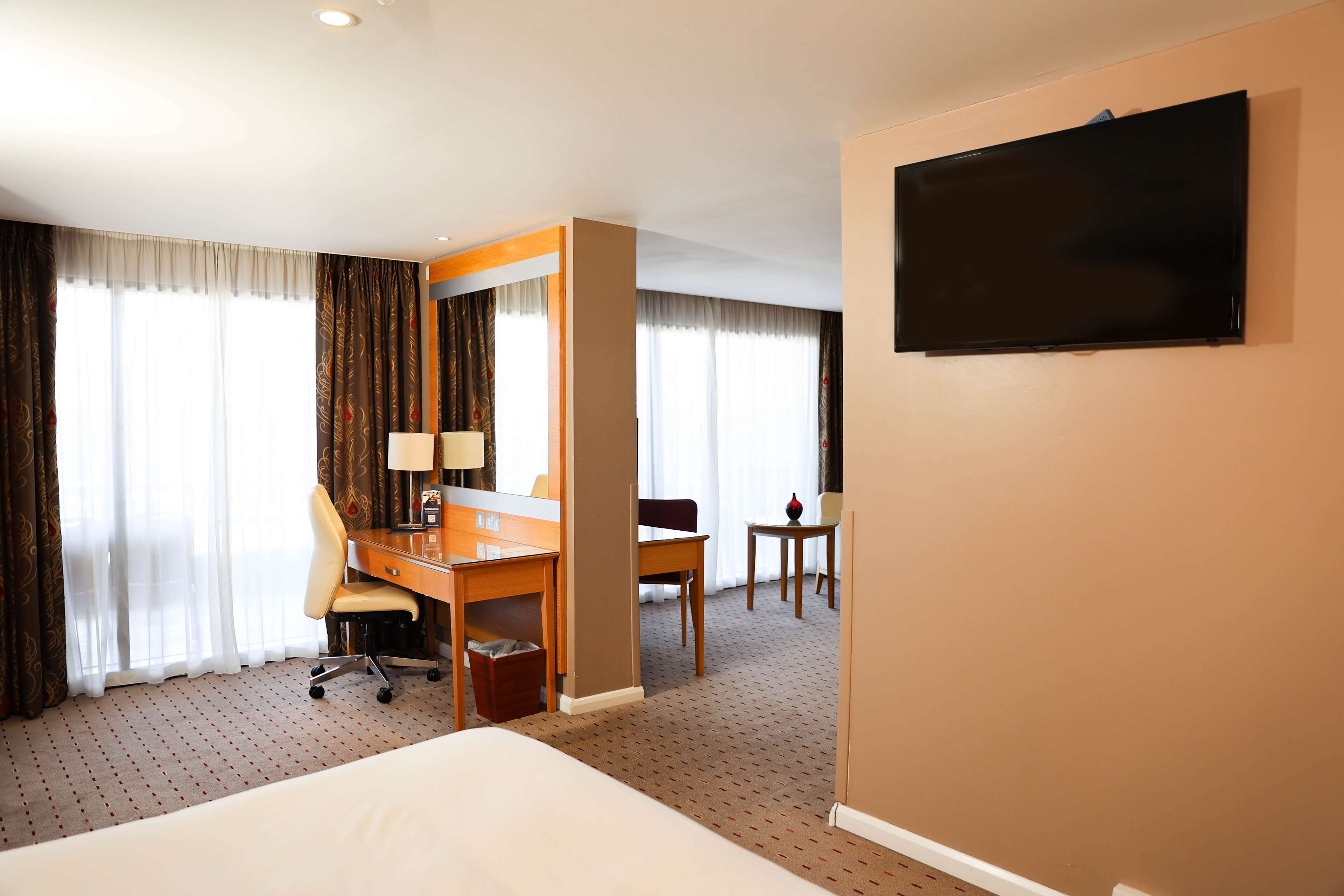 Une chambre d’hôtel avec un lit, un bureau, une chaise, une télévision et une fenêtre avec des rideaux.