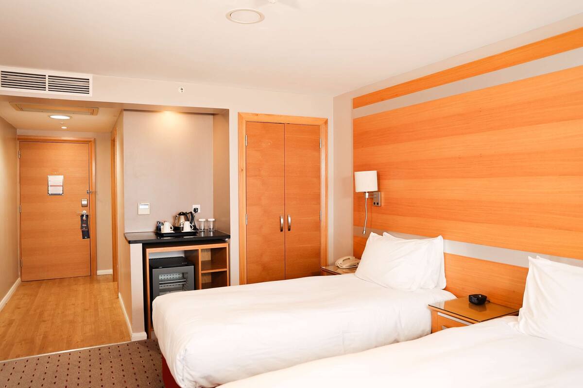 A hotel room with two beds, a desk, a wardrobe, and a minibar.