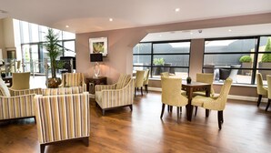A spacious lobby with striped armchairs, a dining area with yellow chairs, and large windows offering views of the outdoors. - DoubleTree by Hilton Milton Keynes (Milton Keynes)