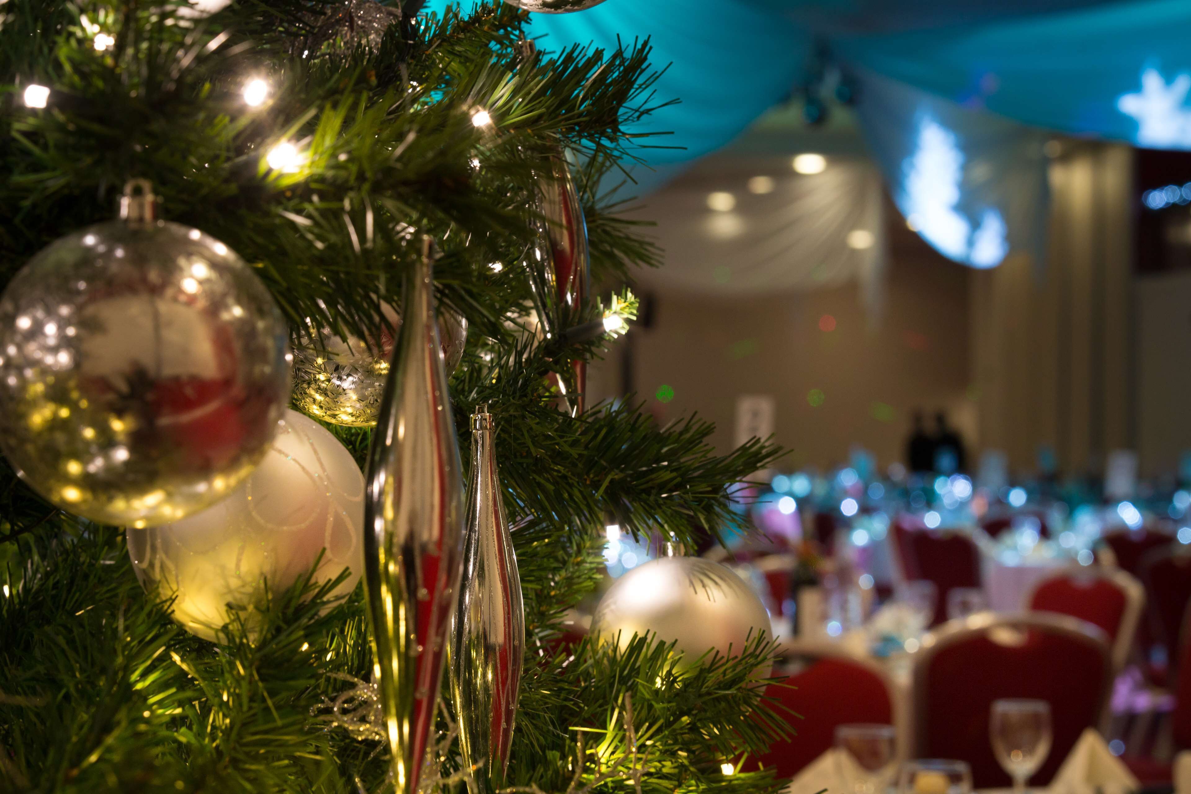 A Christmas tree with ornaments and lights, set in a dining area with tables and chairs.