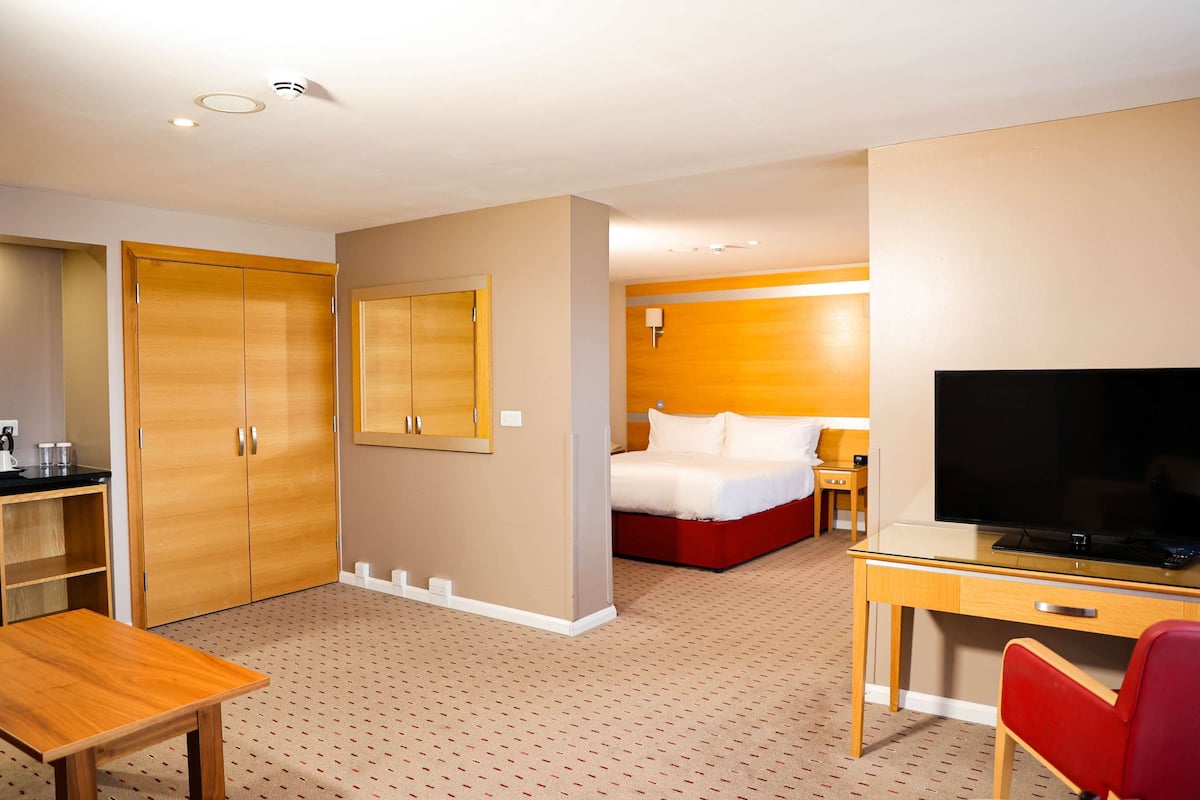 A hotel room with a bed, desk, TV, wardrobe, and a small table.