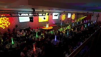 Evento concurrido en interior, con escenario, mesas y asistentes.