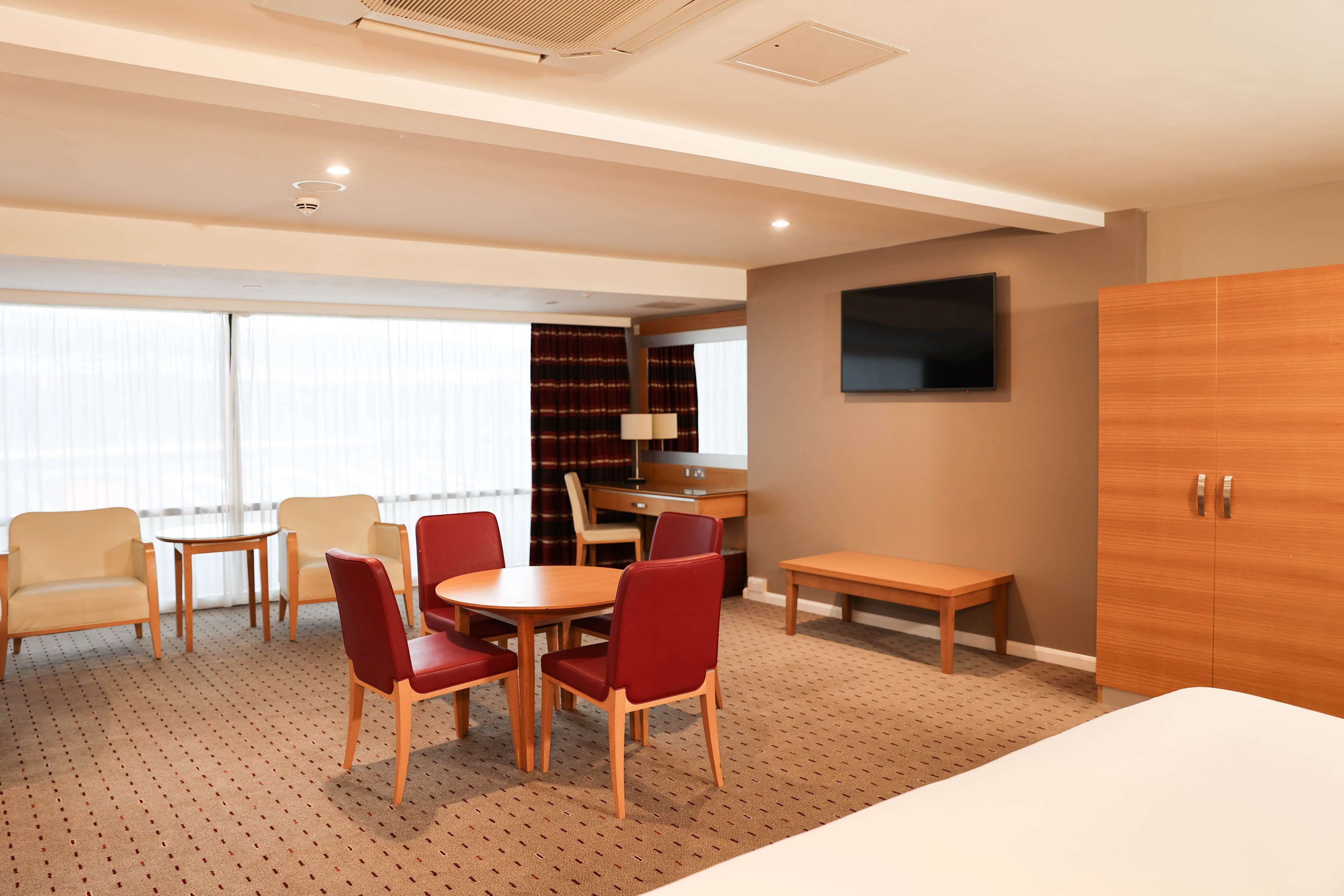 A hotel room with a bed, a desk, a chair, a table, and a TV.
