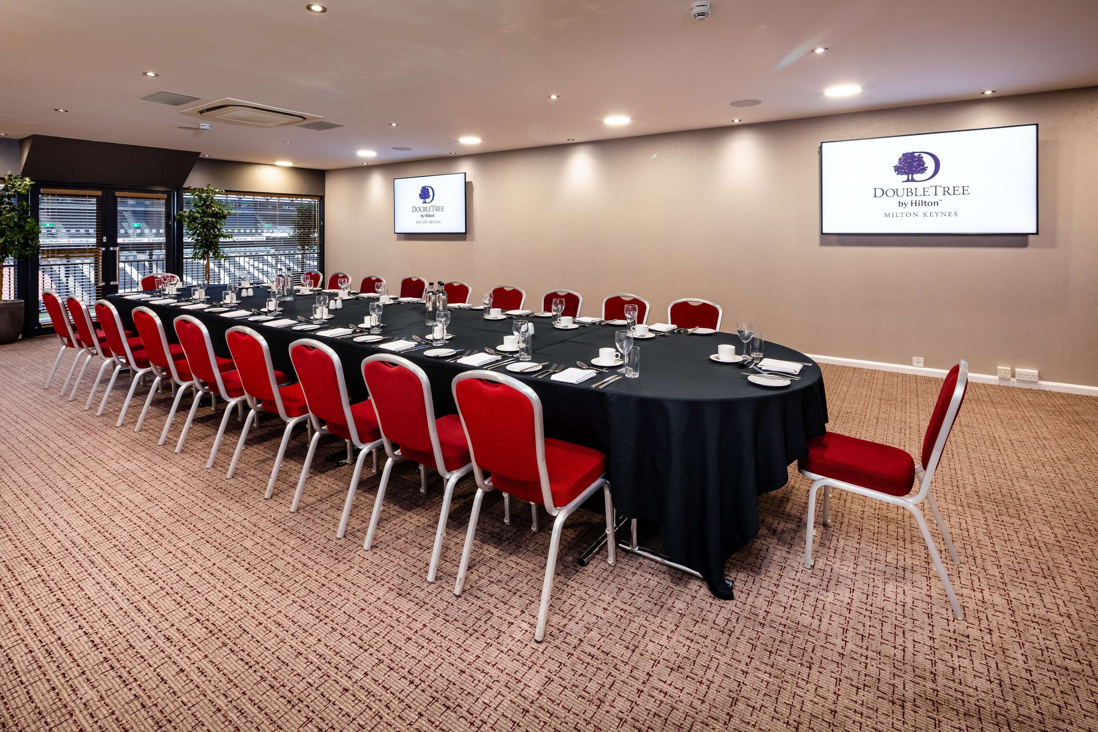 Une salle de conférence avec une longue table, des chaises rouges et deux écrans affichant le logo de DoubleTree.