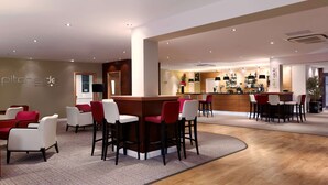 A modern bar area with red and white bar stools, a wooden counter, and a seating area with red and white chairs. - DoubleTree by Hilton Milton Keynes (Milton Keynes)