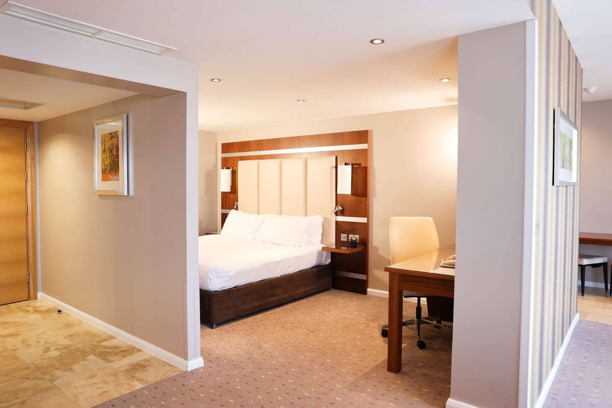 A hotel room with a bed, bedside table, chair, and a desk with a chair.