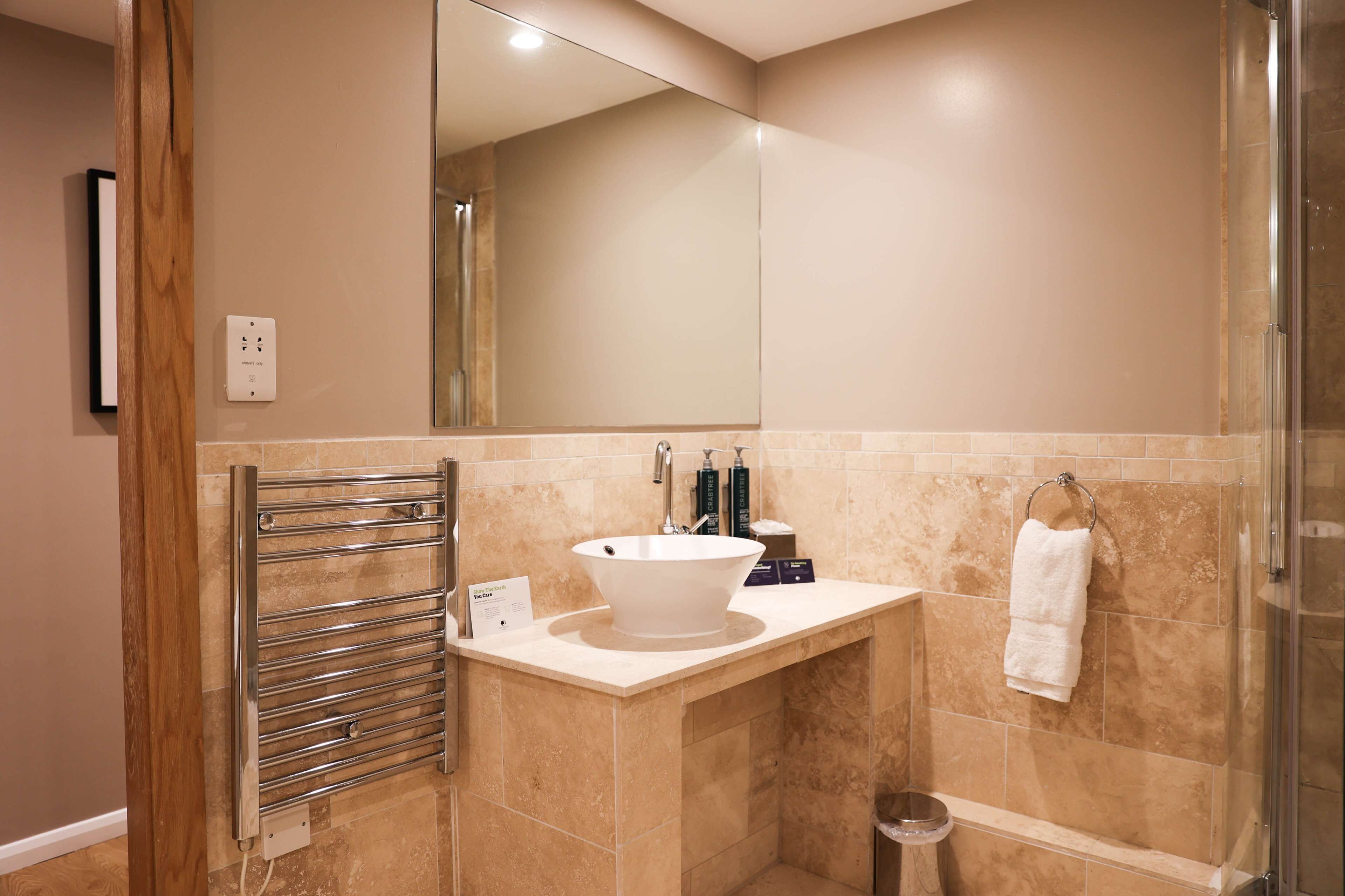Un baño con un espejo grande, un lavabo blanco, un perchero para toallas y una zona de ducha.