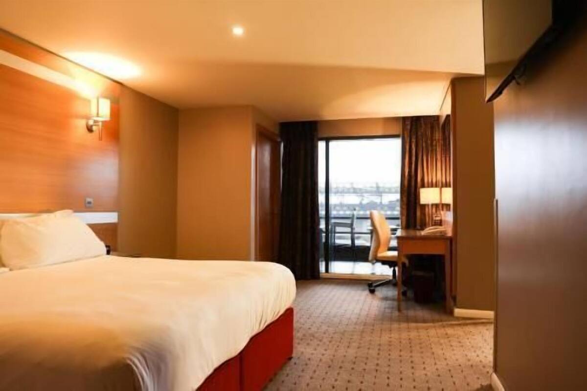 Habitación de hotel con cama, escritorio y vista a la ciudad por la ventana.