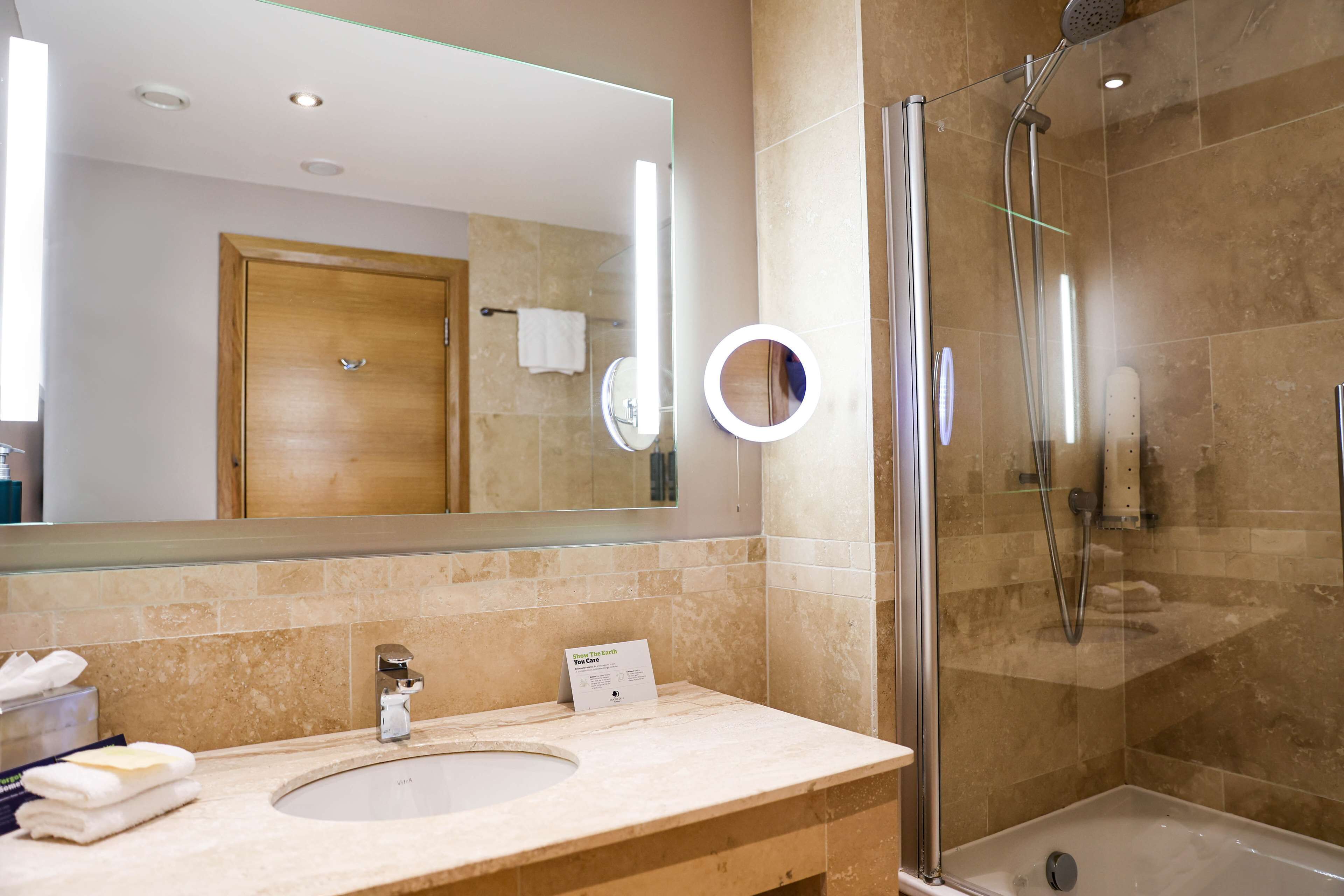 Une salle de bain avec un grand miroir, un lavabo, une douche et une porte en bois.