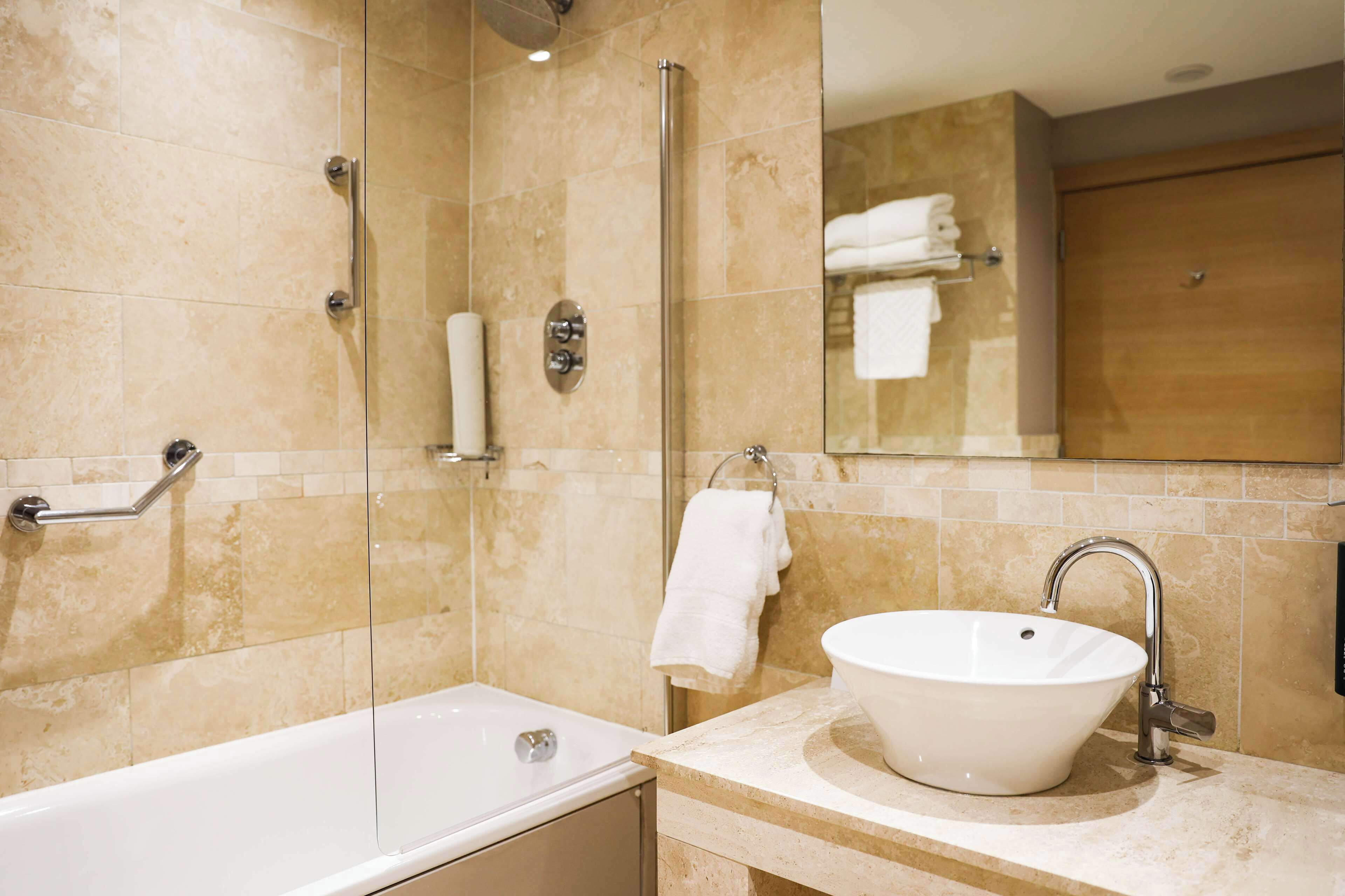 A modern bathroom with a glass-enclosed shower, a white bathtub, and a sink with a mirror above it.