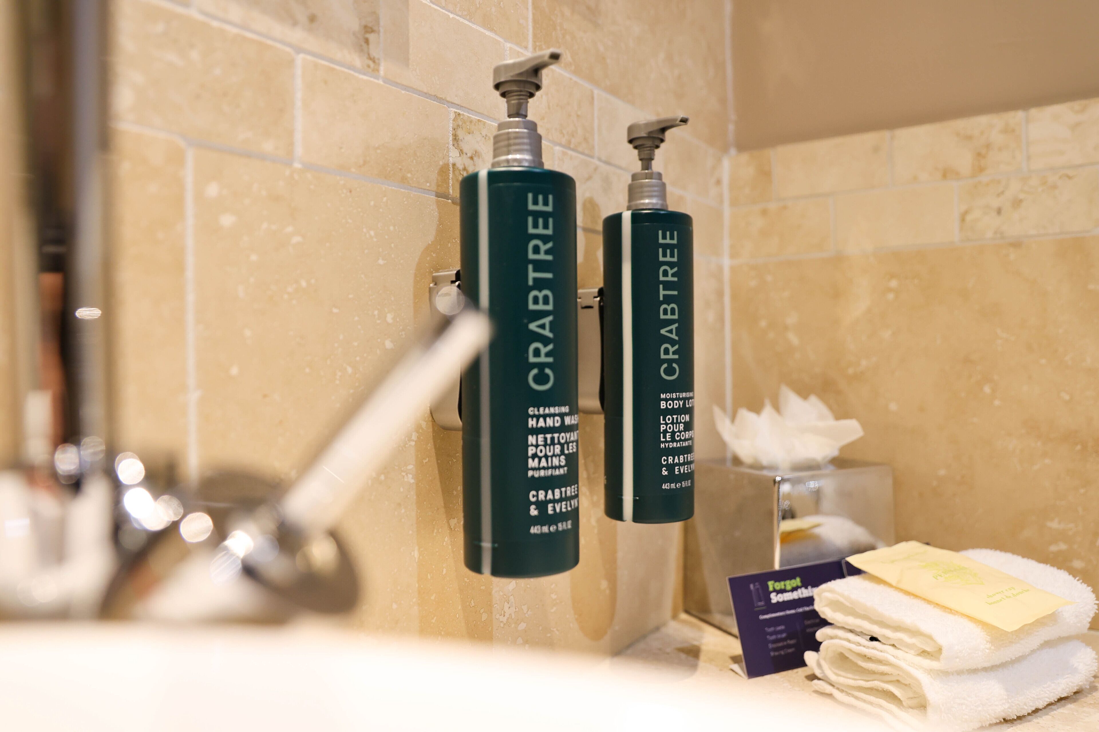 A bathroom with two bottles of Crabtree hand wash and body lotion, a towel dispenser, and a tissue box.