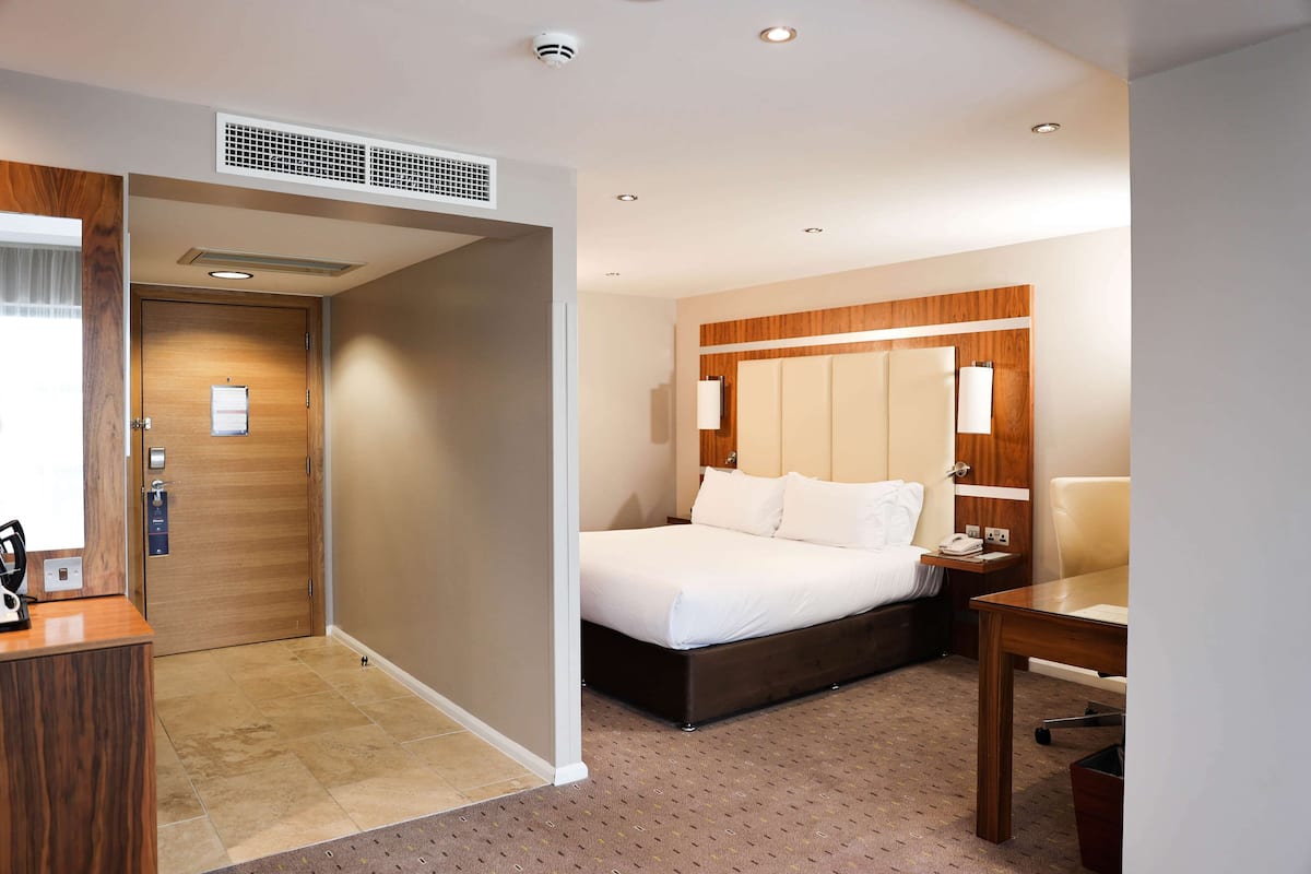 A hotel room with a bed, bedside table, and a desk with a chair.