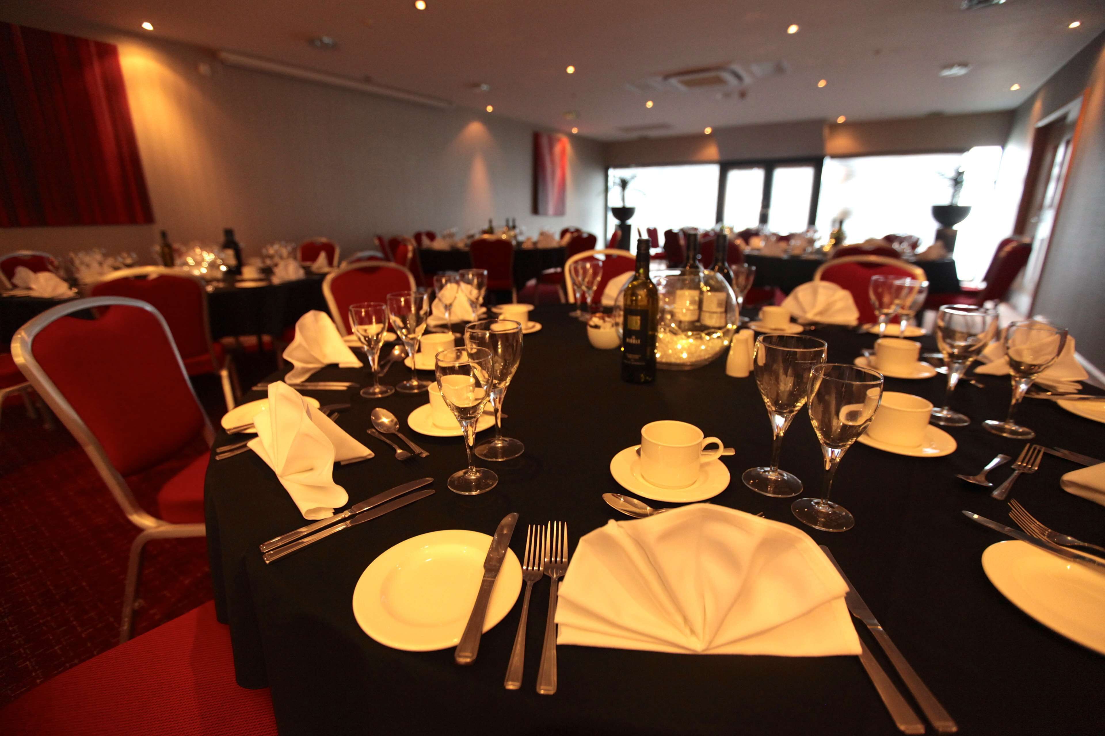 A banquet hall with tables set for dining, featuring white tablecloths, plates, cutlery, and wine glasses.
