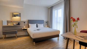 Habitació d'hotel amb un llit, una taula de nit, escriptori, cadira i vista a l'exterior.