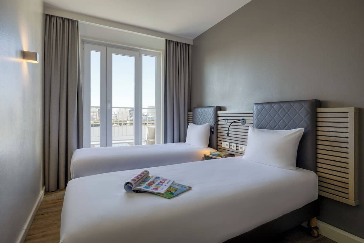 A hotel room with two beds, a large window, and a view of the city.