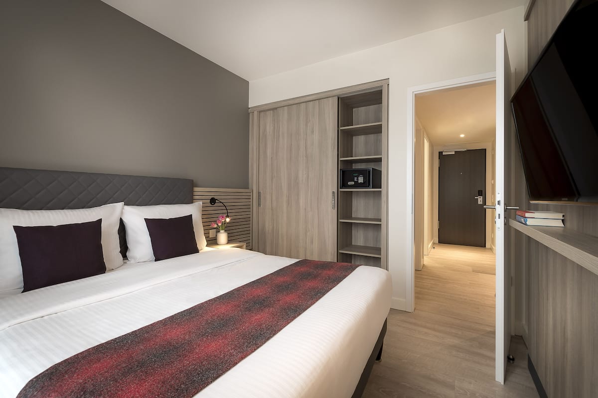 A modern bedroom with a bed, a wardrobe, a TV, and a door leading to another room.