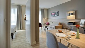 A modern hotel room with a dining area, a sofa, a coffee table, and a bed. - Citadines Arnulfpark Munich (Munich)
