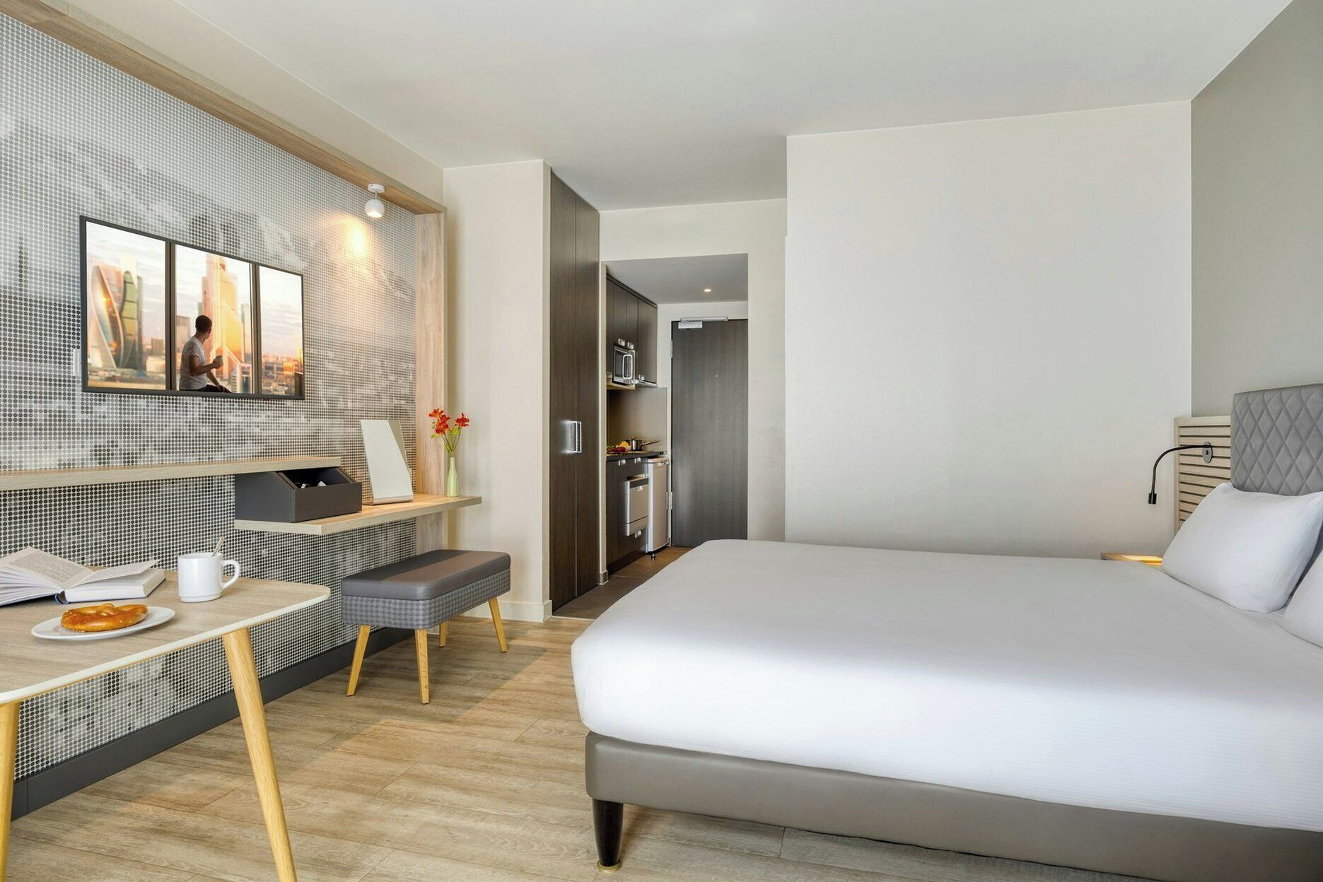 Una habitación de hotel moderna con una cama grande, un escritorio con silla, una kitchenette pequeña y vistas a la ciudad.