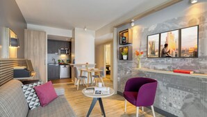 A modern living room with a sofa, a purple armchair, a dining area, and a kitchen. - Citadines Arnulfpark Munich (Munich)