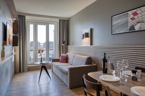 A modern living room with a sofa, dining table, and a city view through large windows.