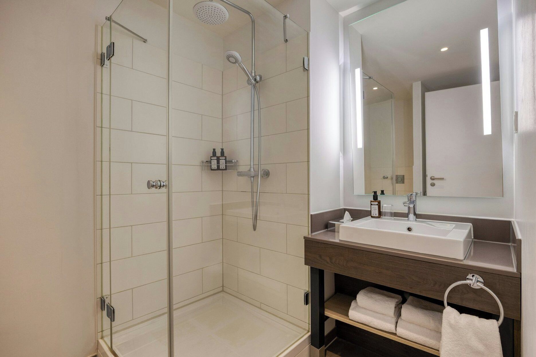 A modern bathroom with a glass-enclosed shower, a large mirror, and a sink with a wooden vanity.