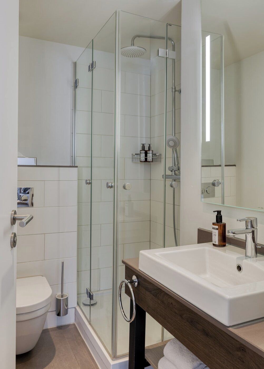 Un baño moderno con cabina de ducha de vidrio, un lavabo blanco y un inodoro.