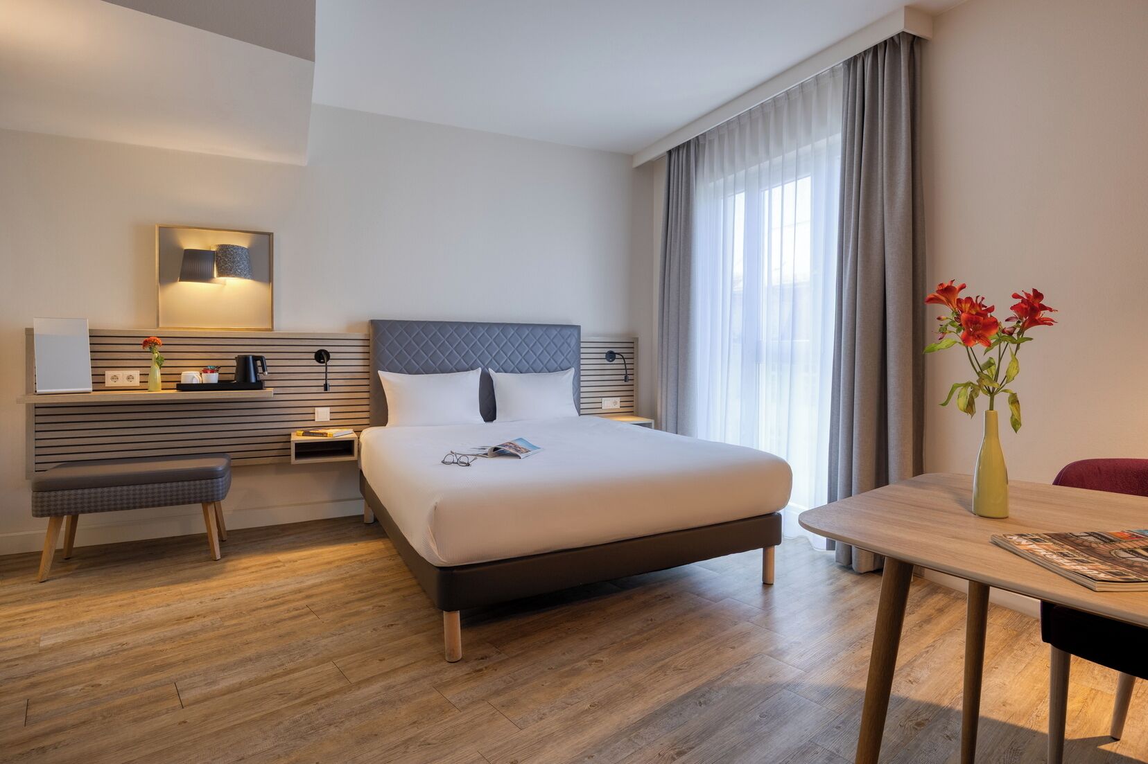 A modern hotel room with a large bed, bedside tables, a desk, and a chair.