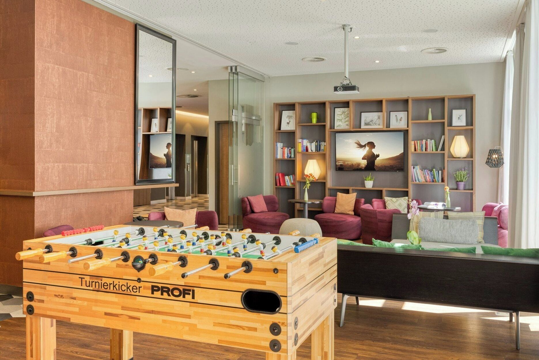 Una habitación con mesa de fútbol, sofá, estantería y televisor.