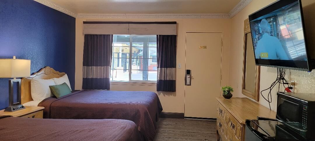Habitación de hotel con dos camas, televisión, escritorio con lámpara y vista al exterior a través de una ventana.