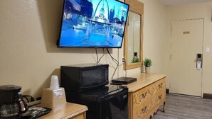 A hotel room with a television mounted on the wall, a wooden dresser, a microwave, a coffee maker, and a bed with patterned bedding.